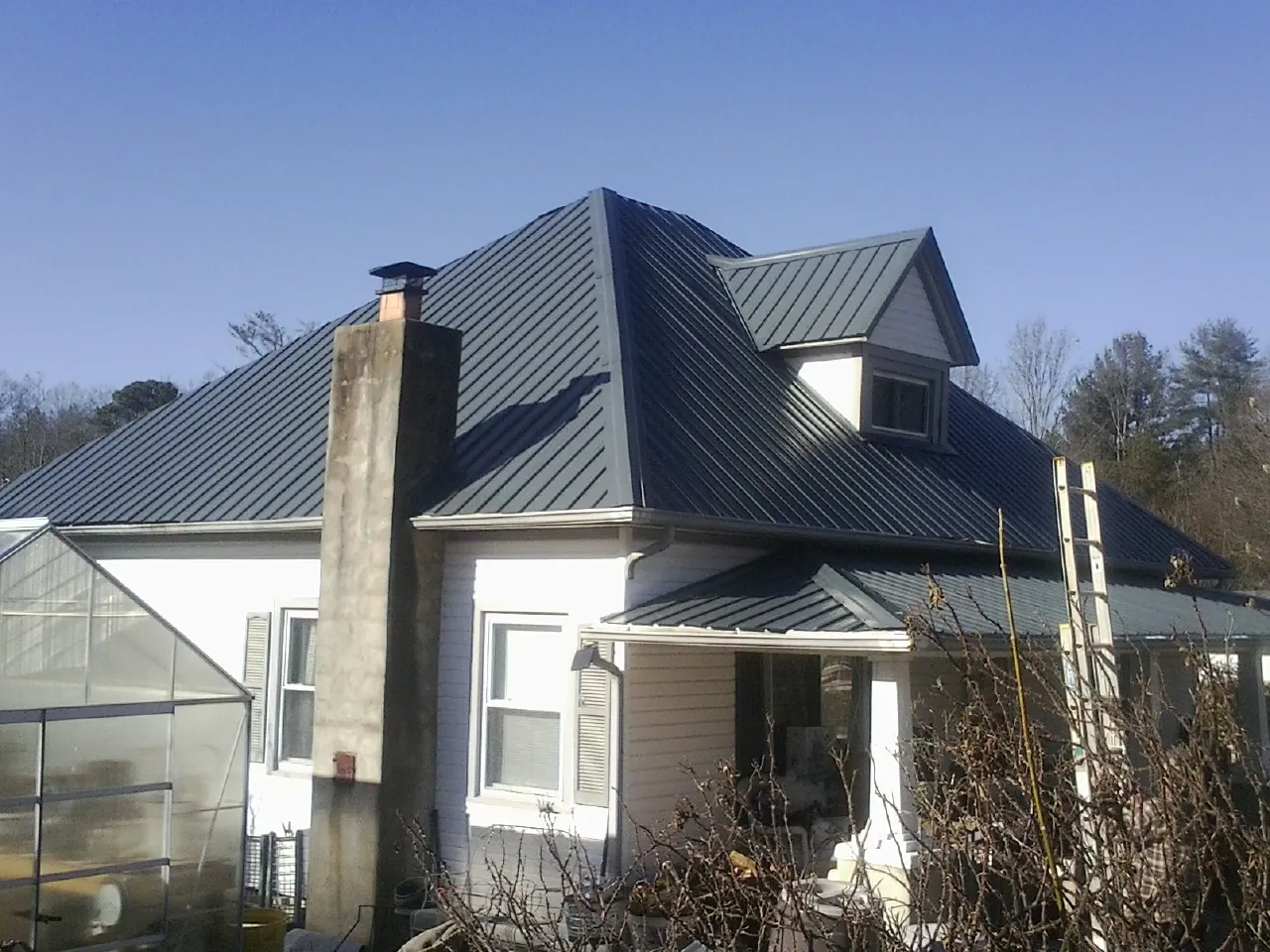 Dark blue standing seam metal roof on a white farmhouse with dormer — Slate & Tile Roof Repair by Roofing Brothers in Mound Valley
