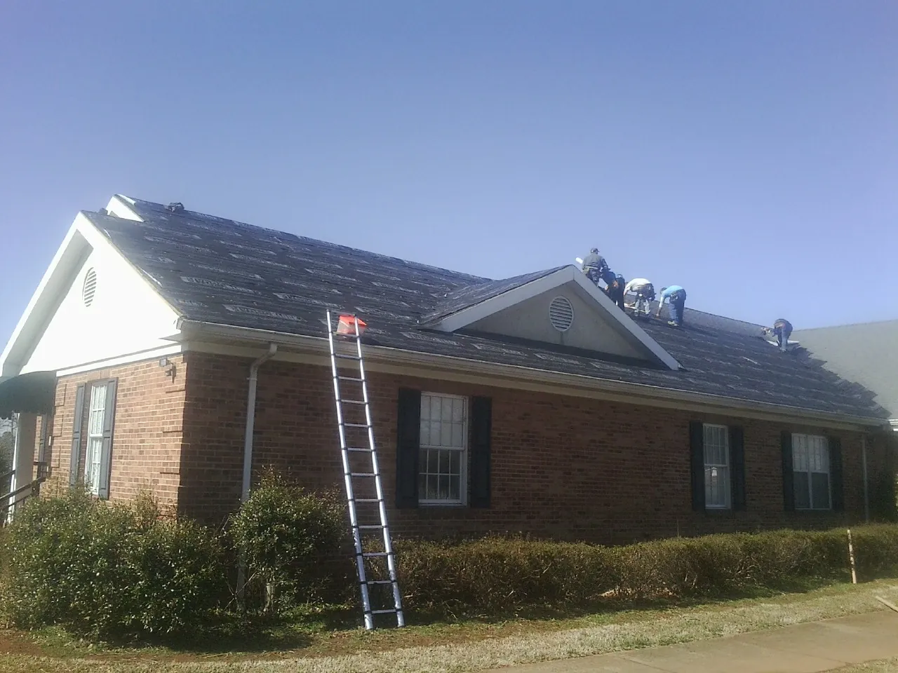 Crew tearing shingles off a brick ranch roof with a ladder set — Emergency Roof Repair work by our crew in Mound Valley