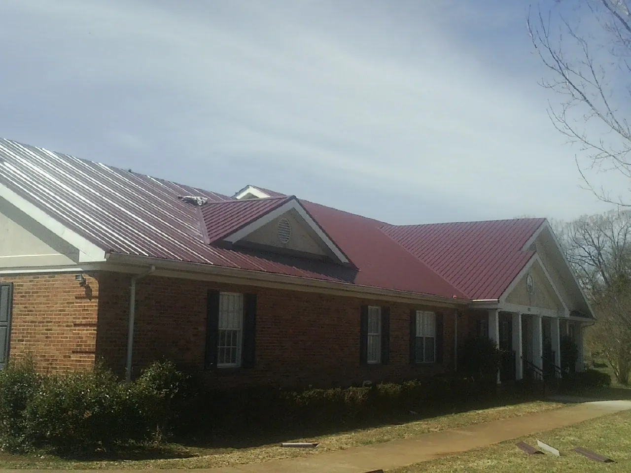 Red metal roof with gabled entries on a long brick building, from a Hail Damage Roof Repair job in Mound Valley