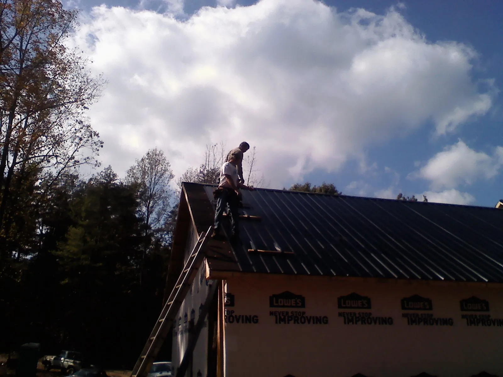 Roofer fastening dark metal panels high against a cloudy sky, from a Roof Inspection job in Mound Valley