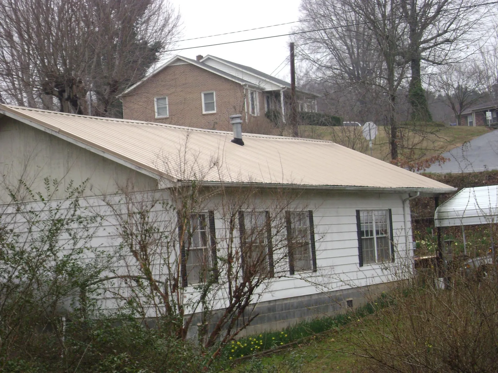 Tan metal roof on a white sided house set into a hillside — Commercial Roofing by Roofing Brothers in Mound Valley