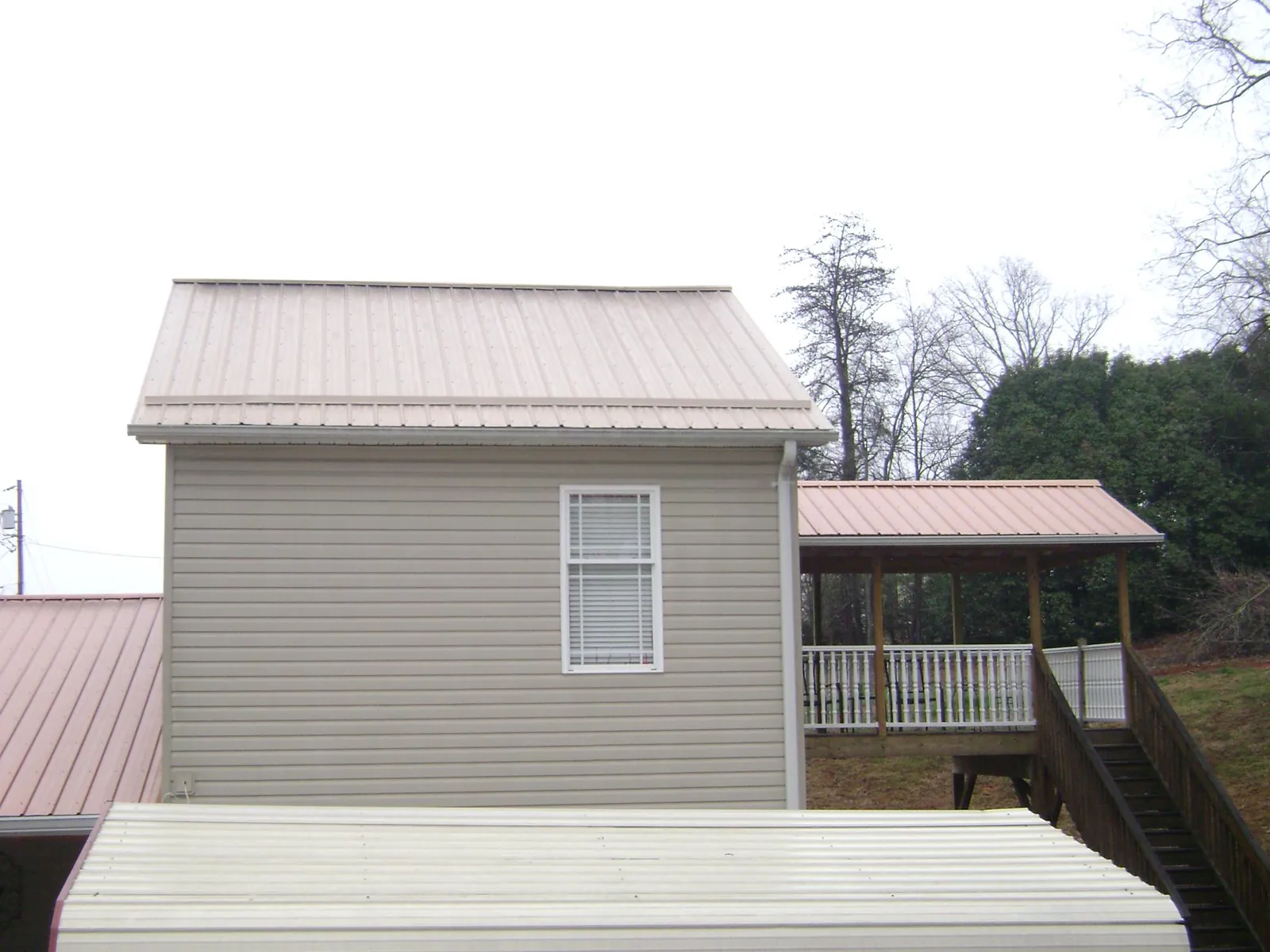 Tan metal roofs on a two story addition and attached porch, from a Roof Replacement job in Mound Valley